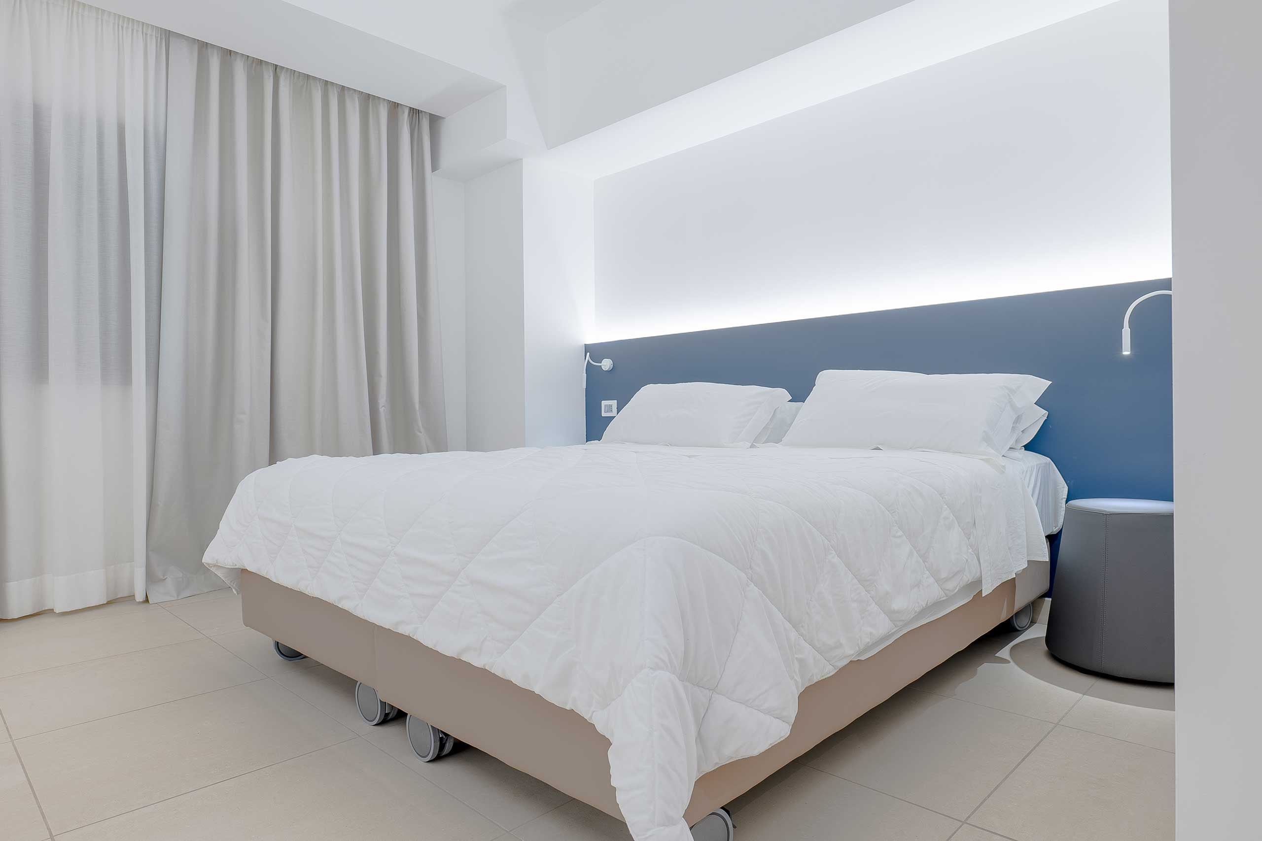 Quarto moderno com cama, cortinas e mesa de cabeceira.