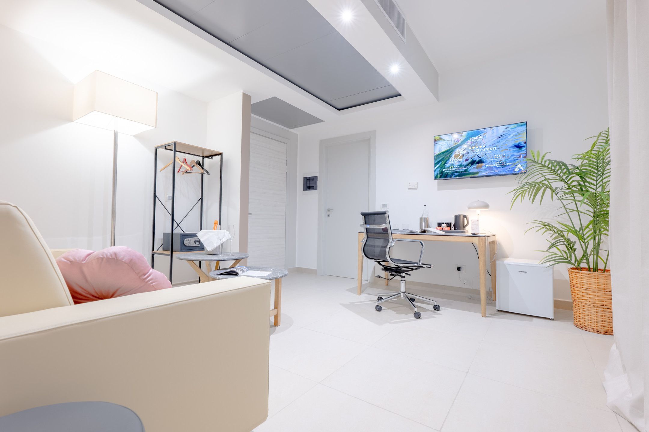 Un espacio de oficina moderno con sofá, escritorio, silla, televisor y planta en maceta.