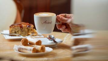 A hand holding a cup of coffee with a logo, a plate with pastries, and a cake on a table.