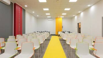 Un salón de conferencias con hileras de sillas blancas, una alfombra amarilla y un pilar rojo a la izquierda.