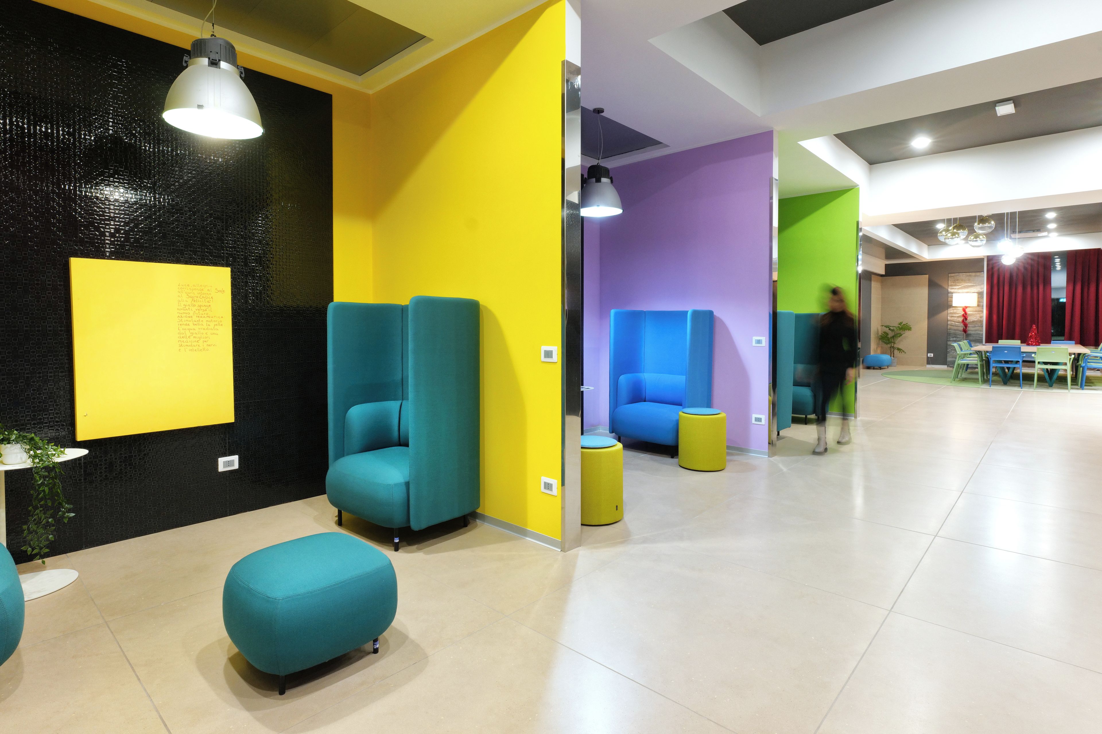 Un interior moderno con asientos turquesa y amarillos, una pared negra con textura y una pared morada con una lámpara de techo.