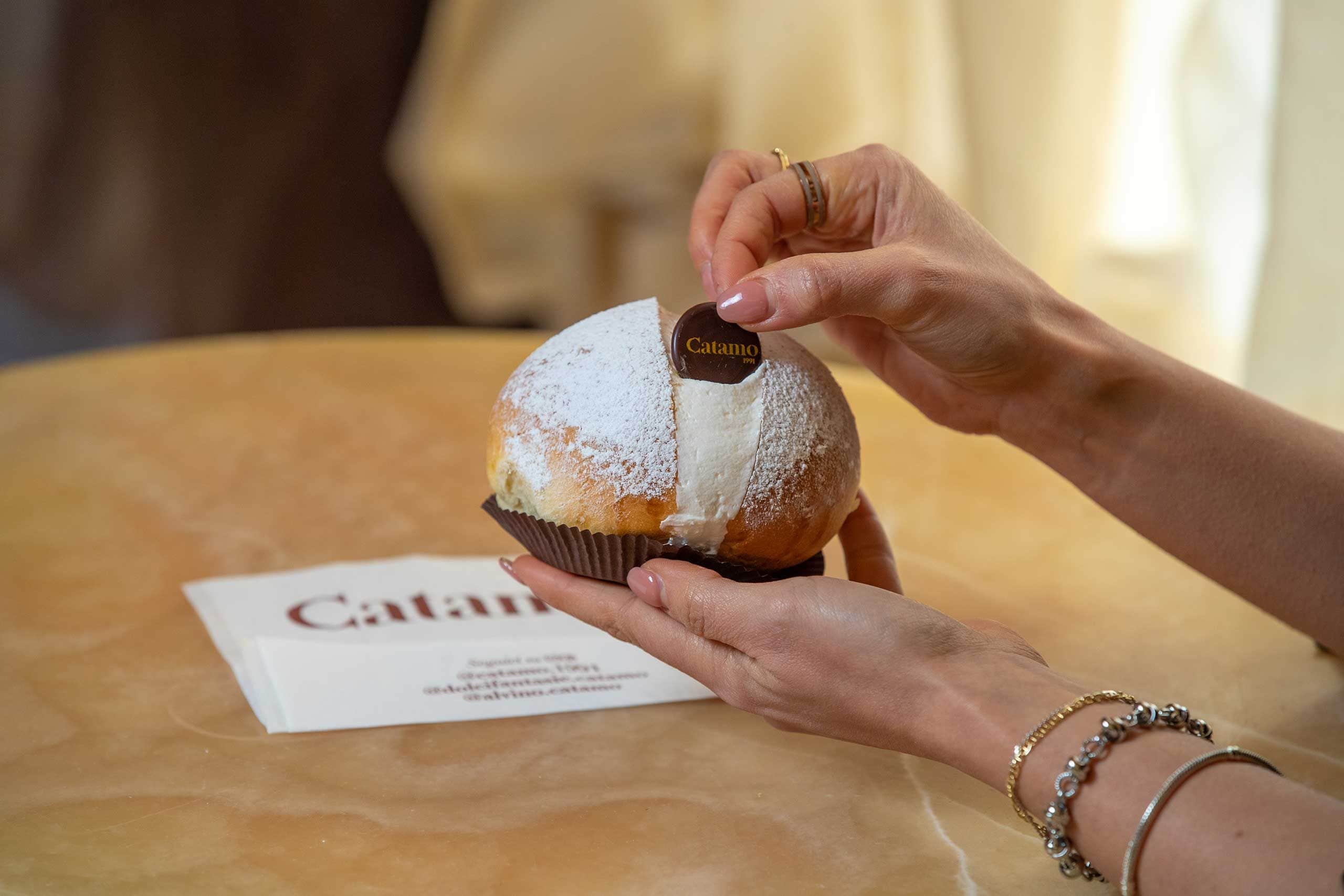 A person holding a Catamo branded pastry with a label, on a table with a menu.