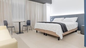 Et moderne hotelværelse med seng, et lille bord med to stole og en sofa.