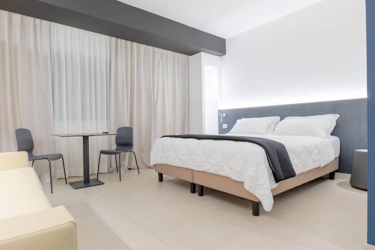 Una habitación de hotel moderna con una cama, una mesita pequeña con dos sillas y un sofá.