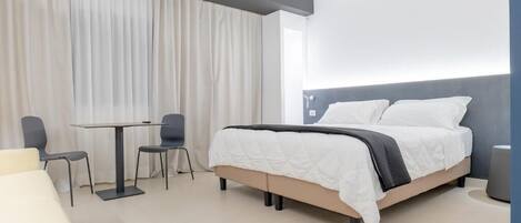 A modern hotel room with a bed, a small table with two chairs, and a sofa.