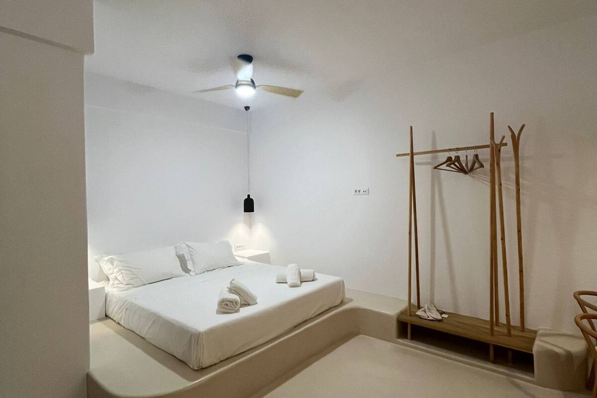 A minimalist bedroom with a bed, a ceiling fan, a nightstand, and a coat rack.