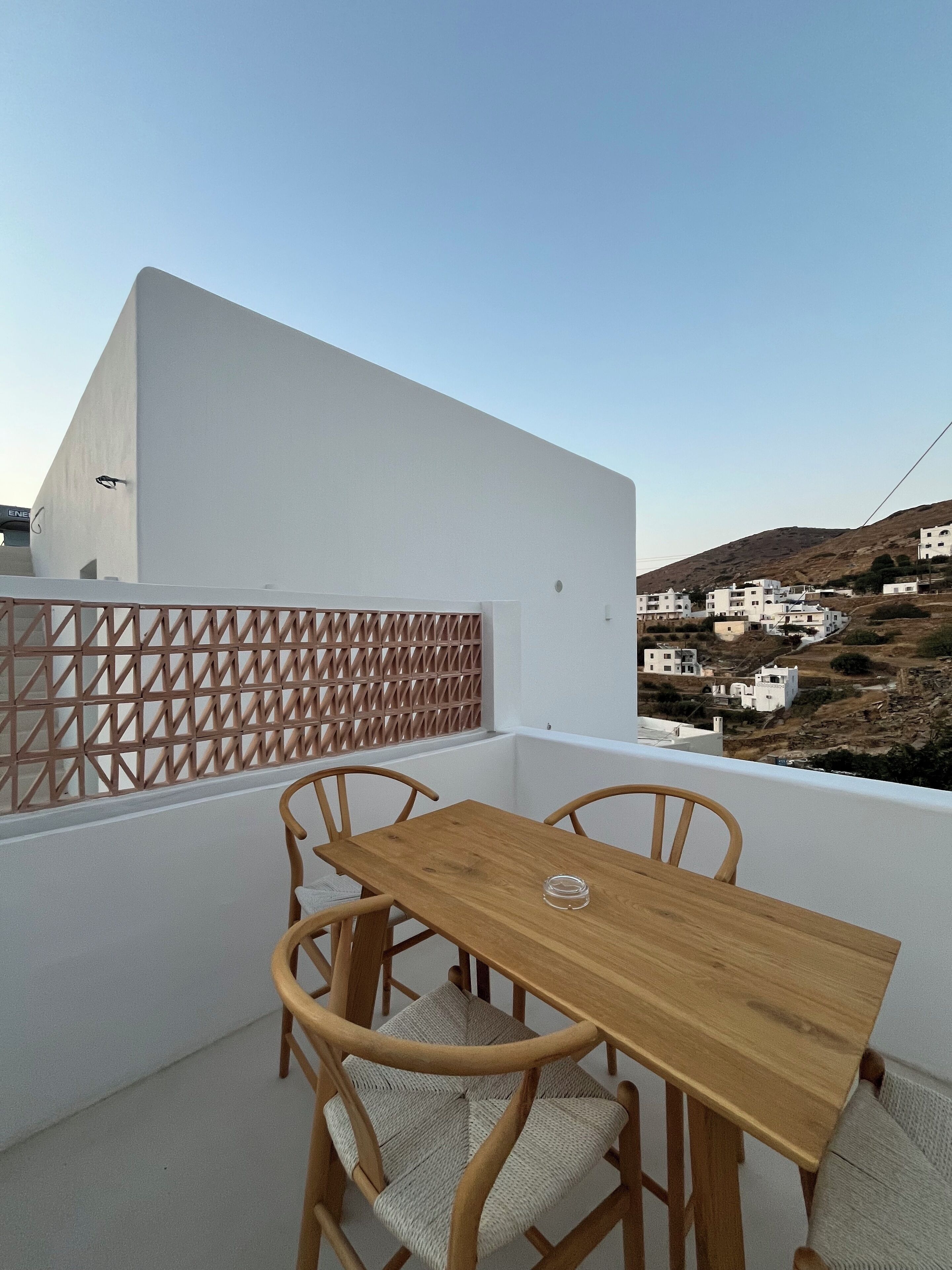 A balcony with a wooden table and chairs, overlooking a hillside with white buildings.