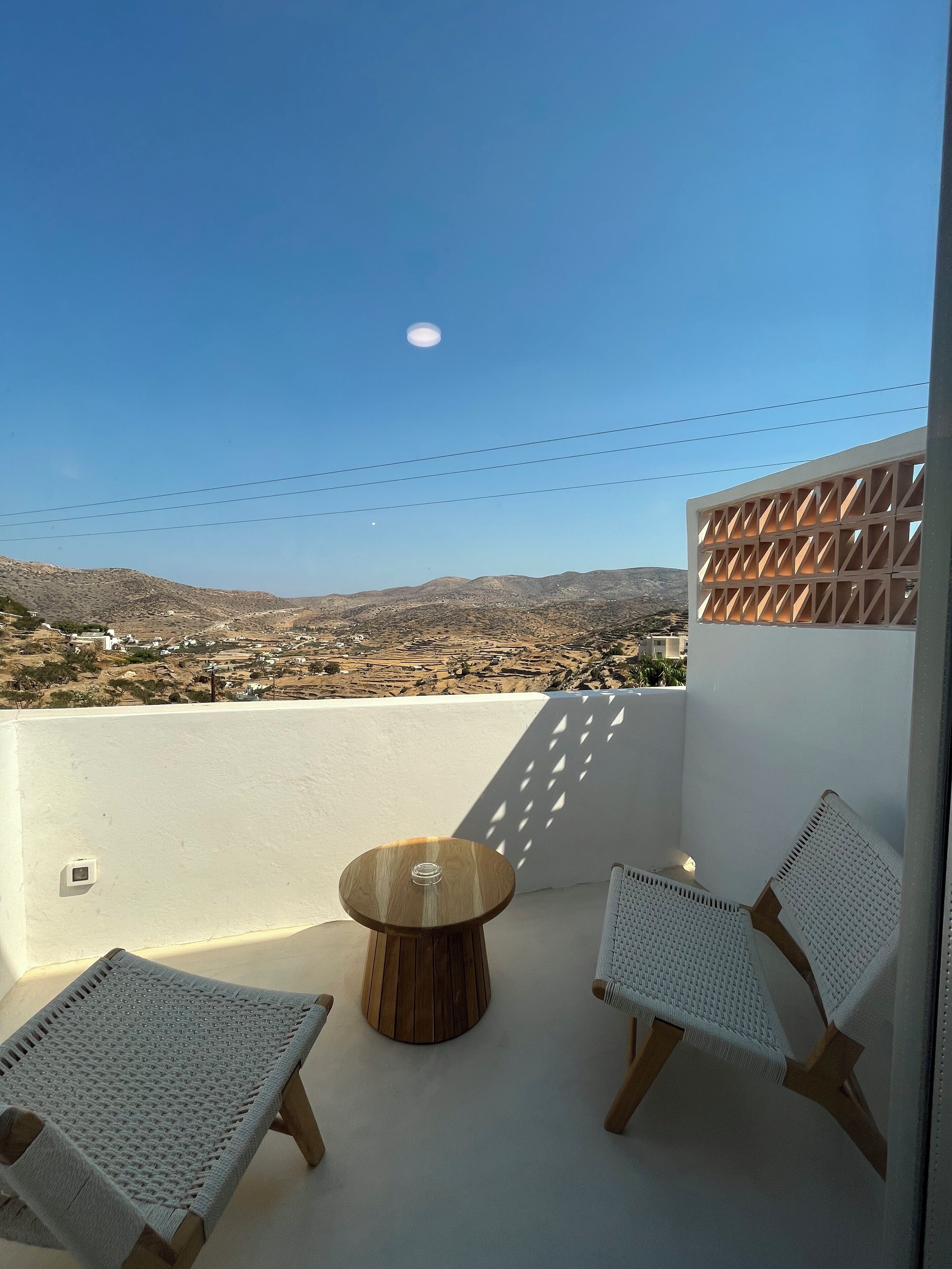 Un balcon avec deux chaises en osier, une petite table en bois et une vue sur un paysage lointain.