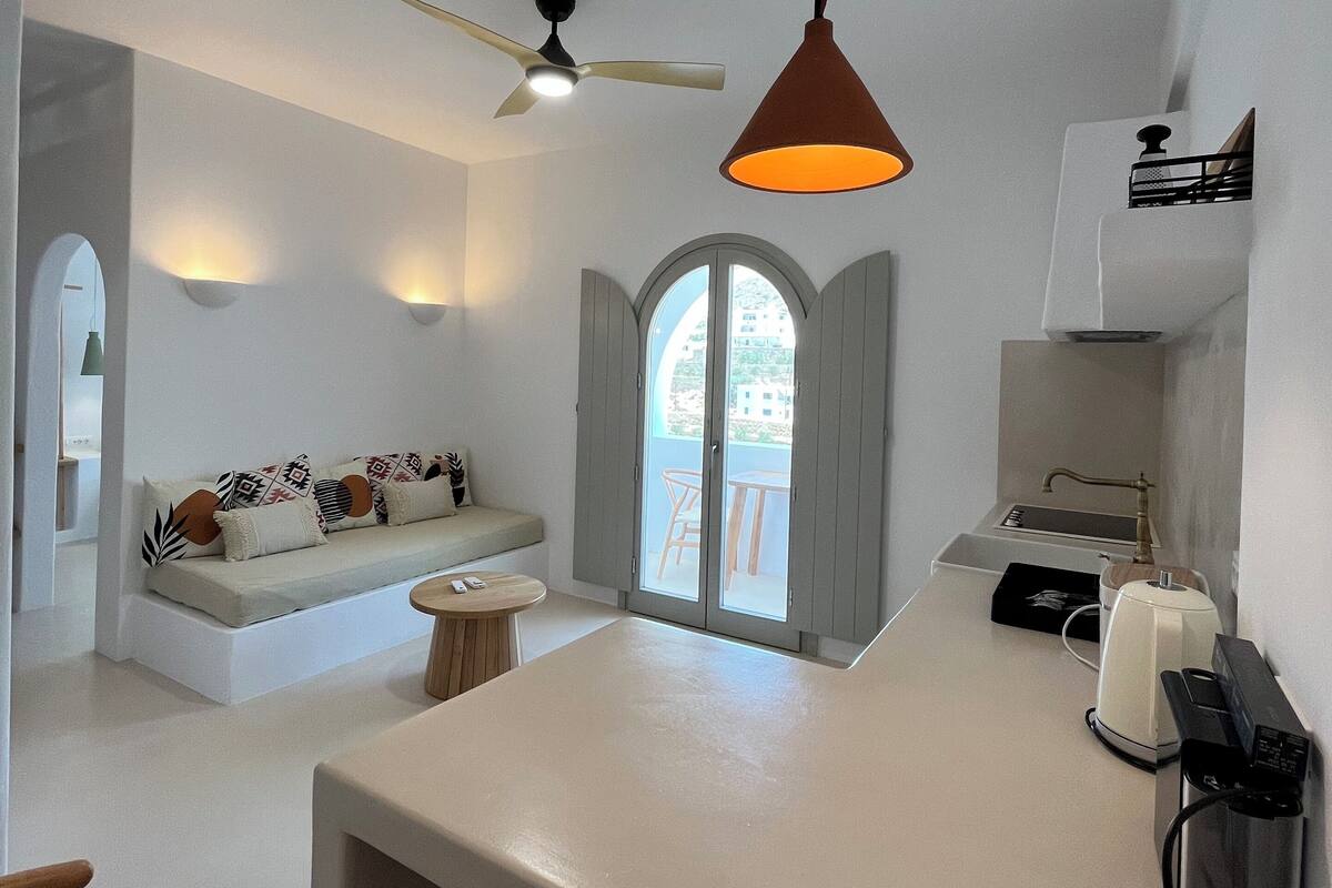 A modern kitchen with a white countertop, a ceiling fan, a hanging pendant light, a built-in sink, and a window with a view of the outside.