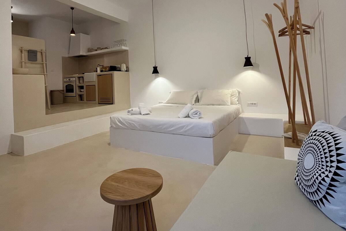 A modern bedroom with a bed, bedside tables, a ceiling fan, and a built-in kitchen area.