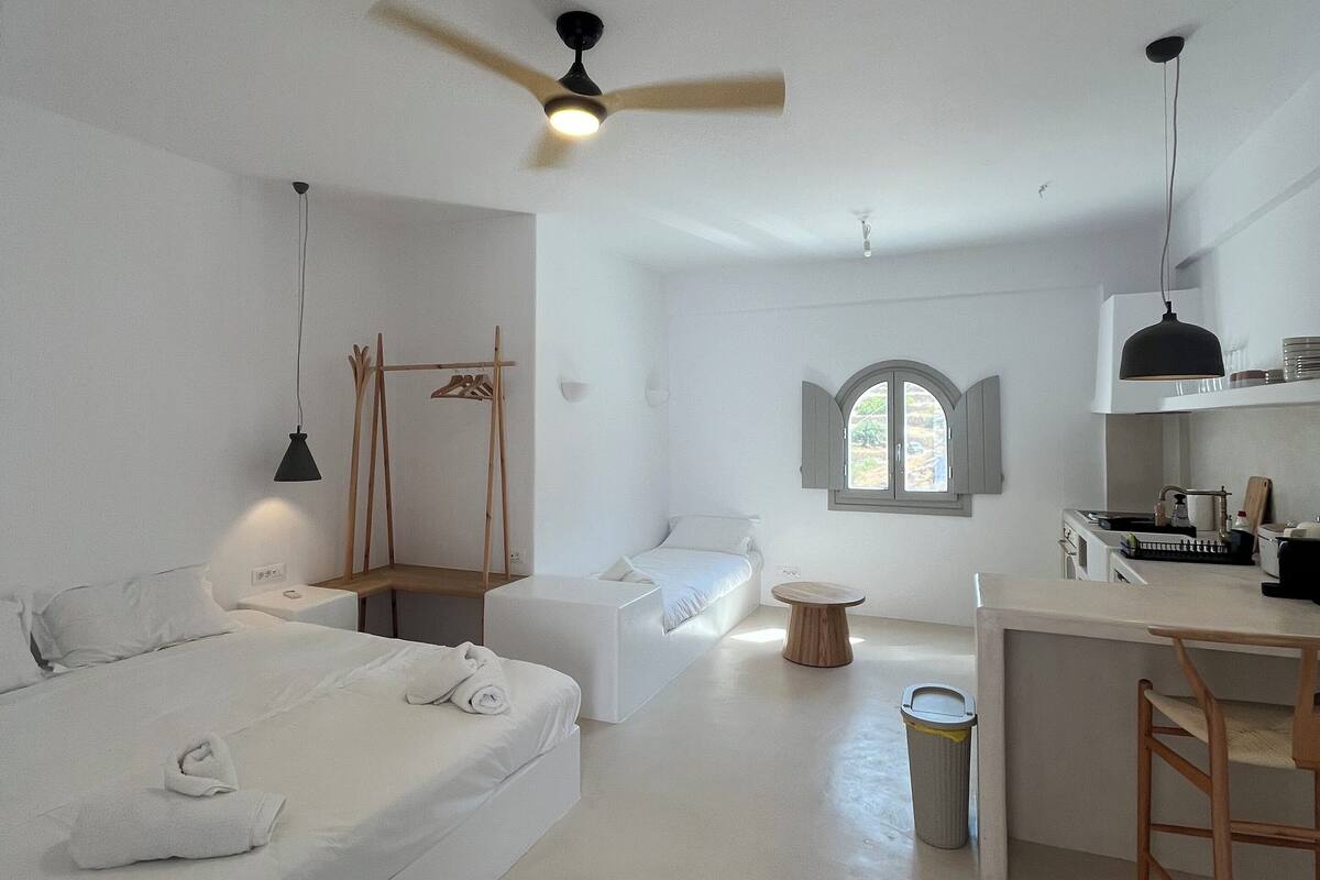 A modern, minimalist room with a bed, a desk, and a small seating area.
