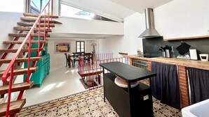 A spacious loft apartment with a high ceiling, a kitchen with a modern stove, a dining area, and a staircase with red railings. - Atypical sunny house - Panoramic terrace at the foot of the Albères (Sorède)