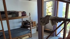 Et værelse med køjesenge, et lille bord og et vindue med udsigt til grøn natur.