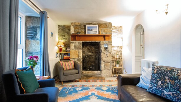 Una sala de estar acogedora con chimenea de piedra, un sillón azul, un sofá de cuero y una alfombra estampada.