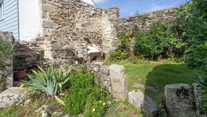 Edificio de piedra con jardín, que incluye un banco de piedra y diversas plantas.