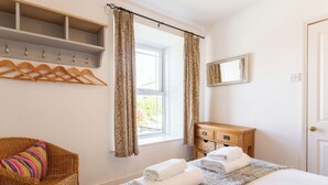 Un dormitorio con cama, una silla, un tocador de madera, un espejo y una ventana con cortinas.