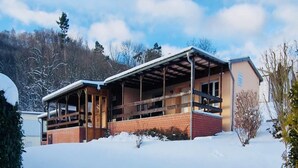 Een gebouw met twee verdiepingen, voorzien van een overdekte veranda en een gevel van baksteen, omgeven door sneeuw en bomen.