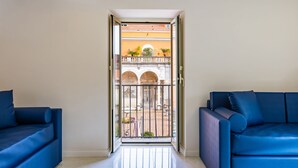 A modern living room with a large sliding glass door leading to a balcony with a view of a building with arches and potted plants. - Palazzo Maddaloni Sweet Home By Napoliapartments (Naples)