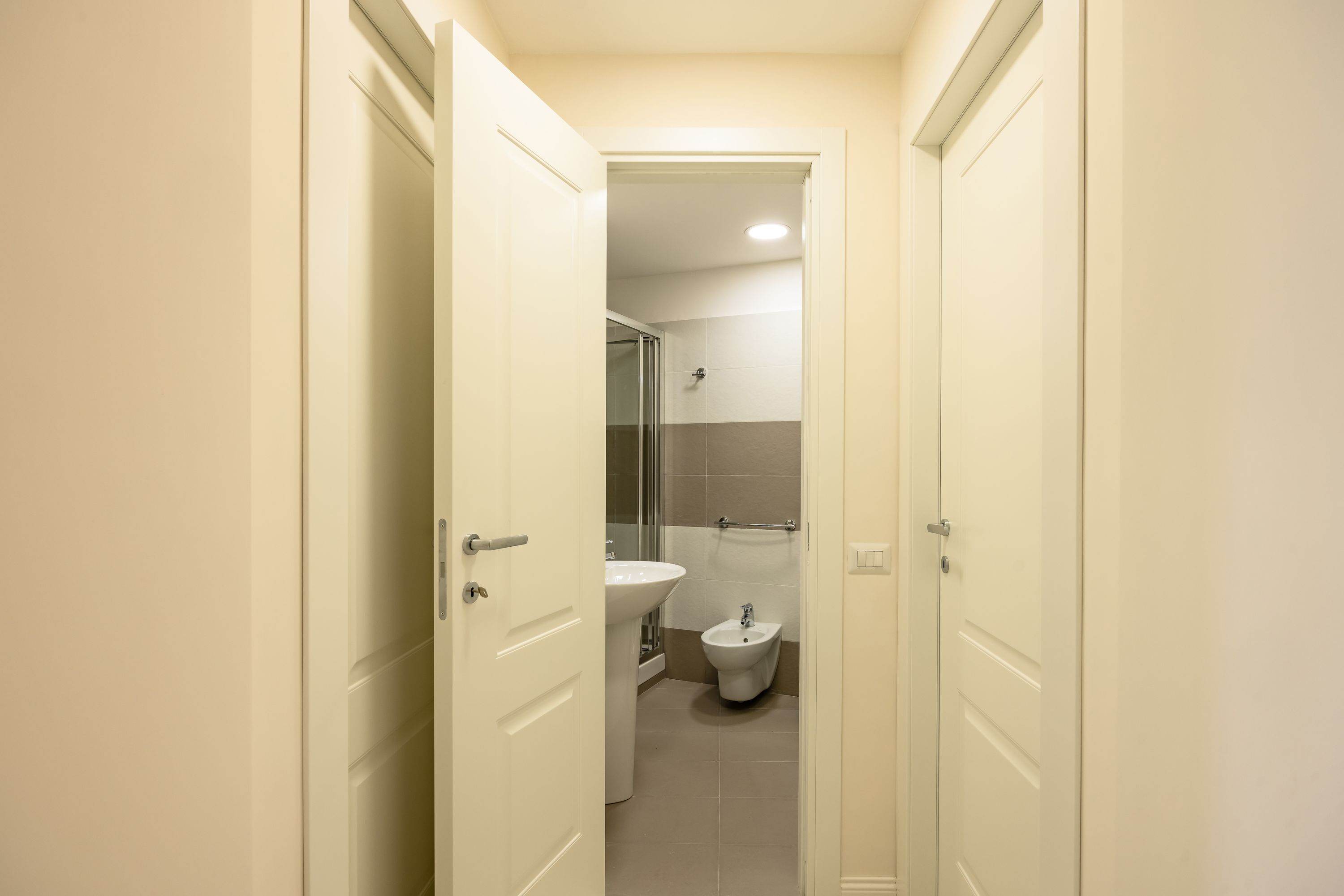 Ein schmaler Flur, der zu einem Badezimmer mit Toilette, Bidet und Waschbecken führt.