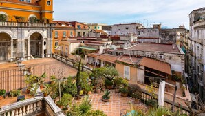 A courtyard with a tiled floor, surrounded by buildings with balconies and potted plants. - Palazzo Maddaloni Sweet Home By Napoliapartments (Naples)