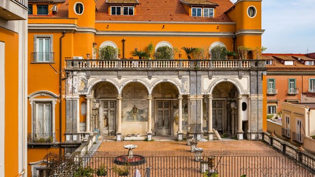 A courtyard with a fountain, arches, and a building with a yellow facade and red roof. - Palazzo Maddaloni Sweet Home By Napoliapartments (Naples)