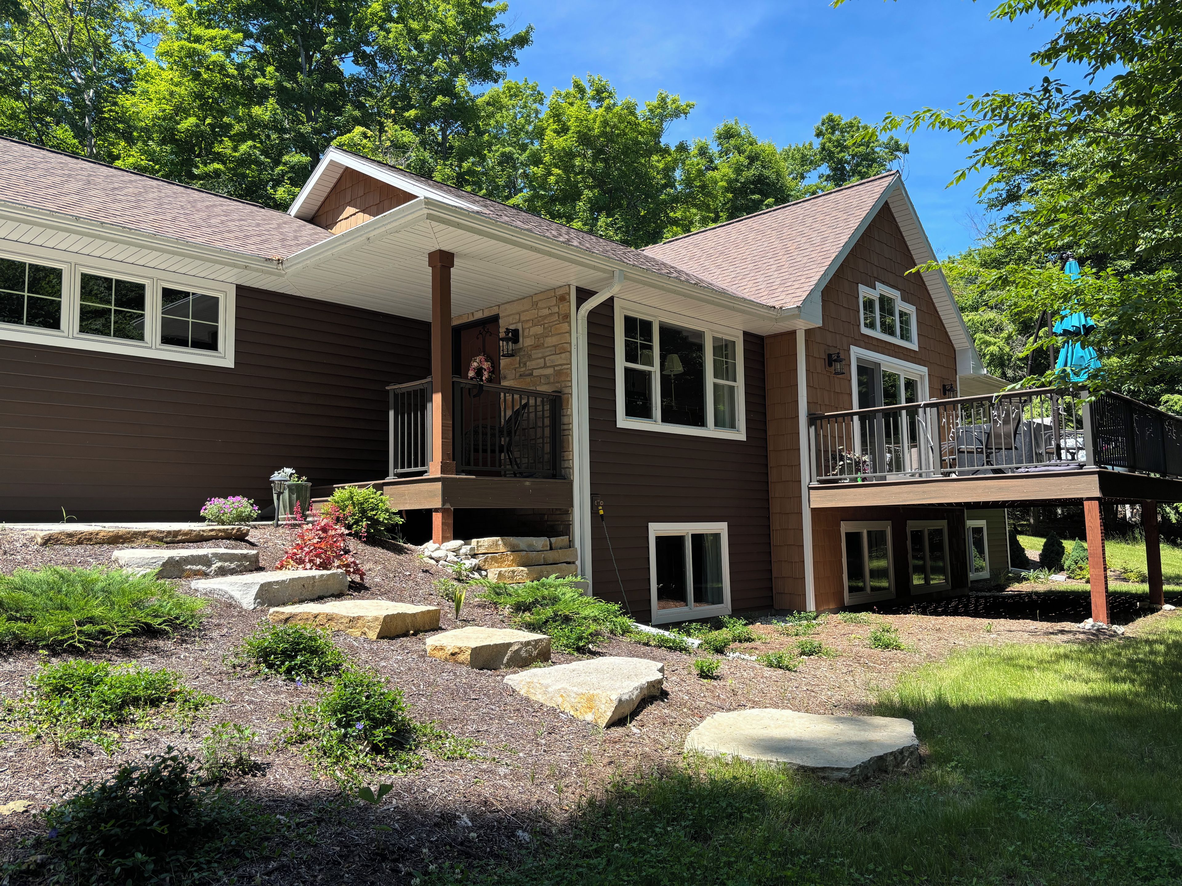A two-story house with a covered porch, stone steps, and a landscaped garden.