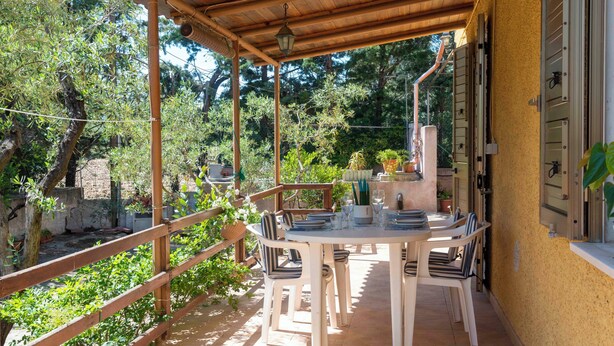 An outdoor patio with a round table and chairs, surrounded by a wooden fence and potted plants.