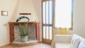 A room with a brick fireplace, a potted plant, a white sofa, and a window with curtains.