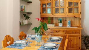 A dining area with a wooden table set for four, surrounded by chairs. There are glassware and plates on the table, and a cabinet with glass doors above it.