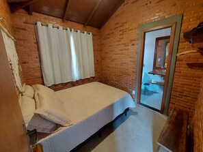 A small, cozy room with a single bed, a window with curtains, a wooden door, and a brick wall. - Villa da Serra Chalé Ibitipoca (Lima Duarte)