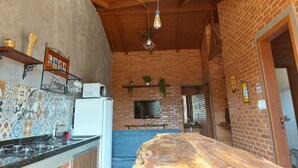 Una cocina con pared de ladrillo, techo de madera y encimera con estufa. Hay un televisor montado en la pared y una ventana con persianas.