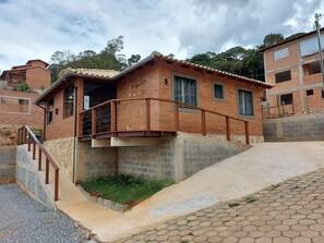 A two-story brick house with a balcony, a small garden, and a paved driveway. - Villa da Serra Chalé Ibitipoca (Lima Duarte)