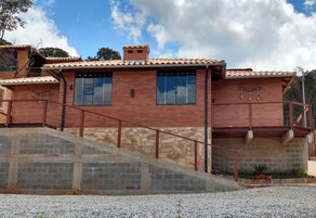 Uma casa de dois andares com fachada de tijolos, janelas amplas e uma escadaria de pedra que dá para uma varanda.