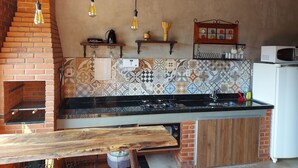 Una cocina con horno de ladrillo, una mesa de madera, bombillas colgantes y un microondas.