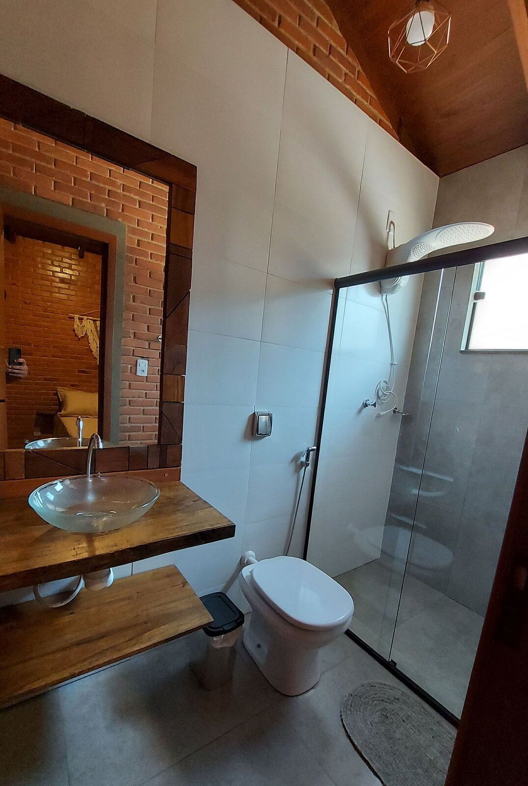 Un baño moderno con ducha envuelta en vidrio, tocador de madera con lavamanos de cristal y un inodoro blanco.
