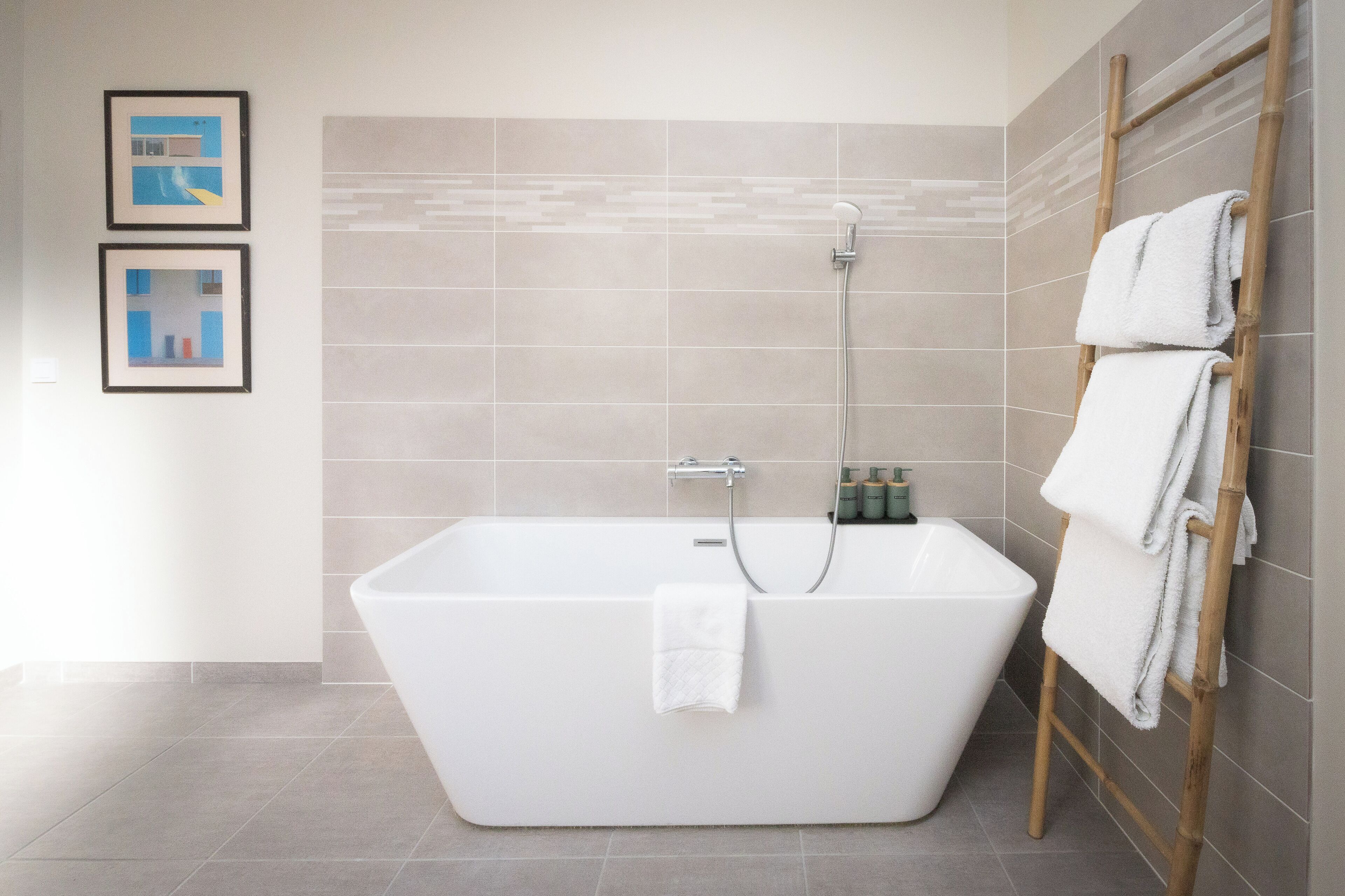 Un baño moderno con una bañera independiente, un perchero de madera y dos cuadros en la pared.
