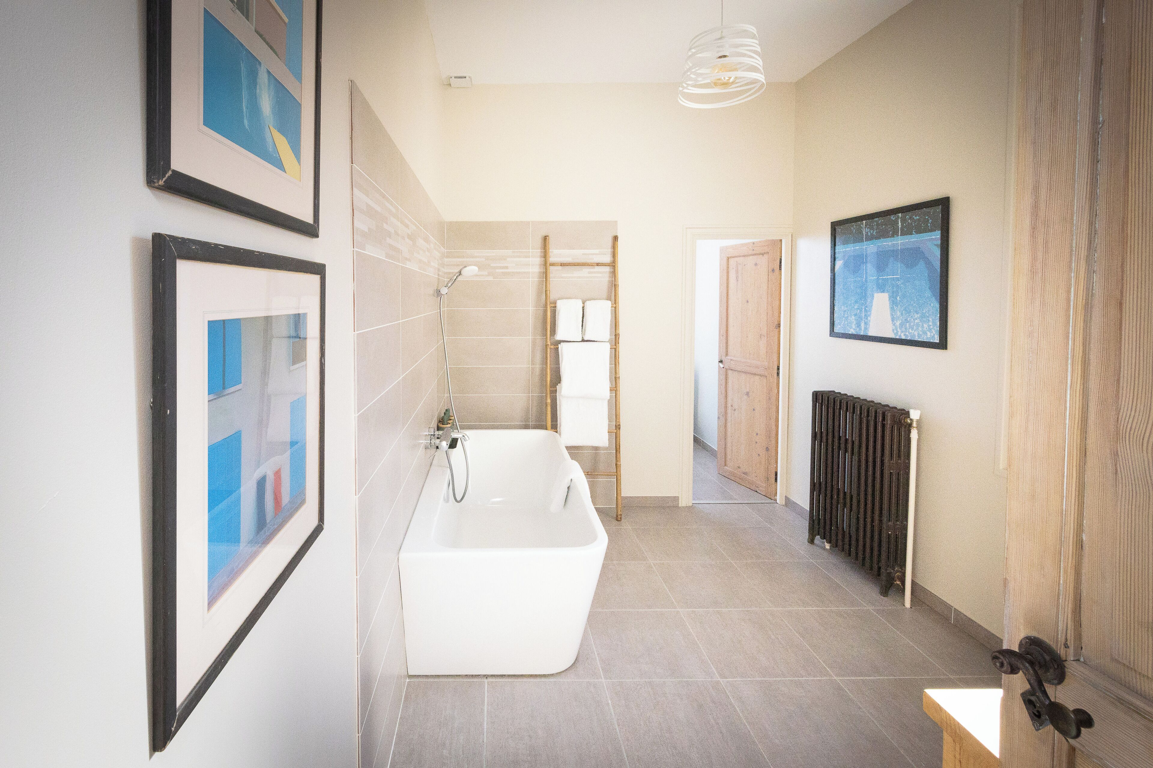 Un baño moderno con una bañera independiente, paredes con azulejos y una obra de arte enmarcada.