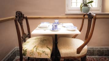 Un coin repas avec une table dressée pour deux personnes, agrémenté de chaises à motifs floraux et de vaisselle bleue et blanche.