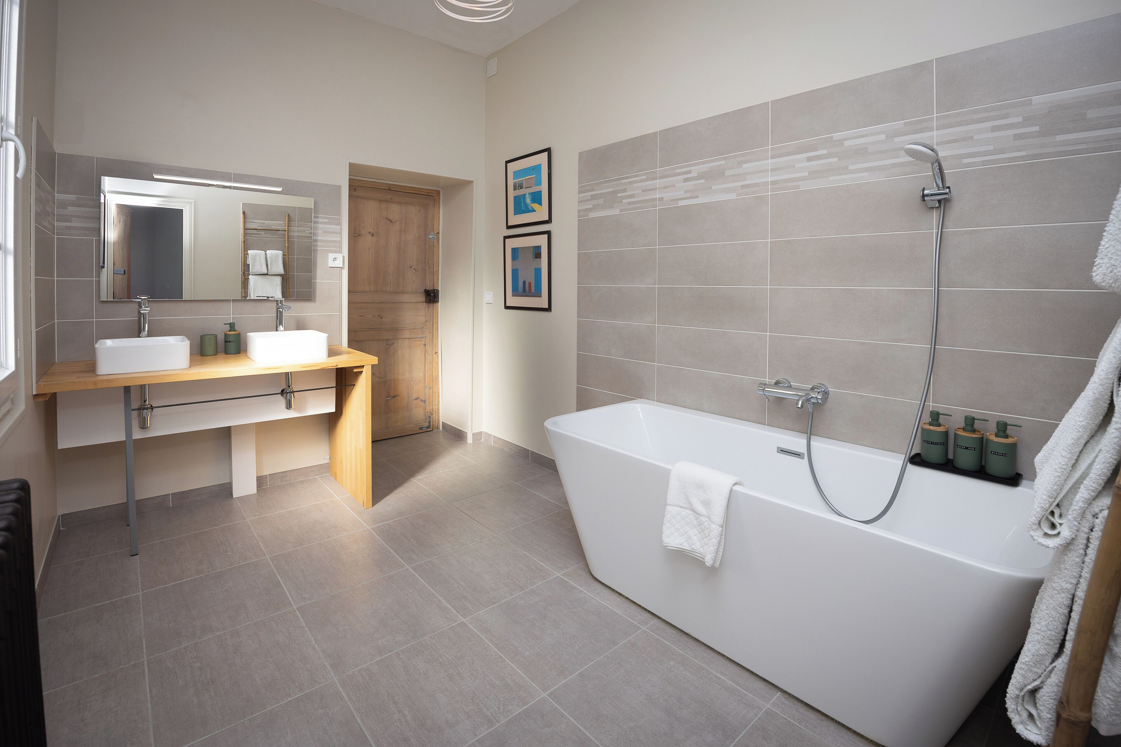 A modern bathroom with a freestanding bathtub, a vanity with a mirror, and two framed pictures on the wall.