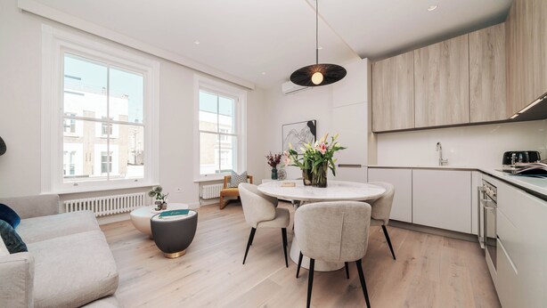 Una cocina moderna con armarios blancos, una mesa de comedor con sillas e iluminación colgante.