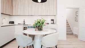 Una cocina moderna con armarios de madera clara, una mesa redonda de mármol y dos sillas.