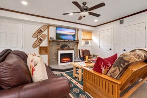 A living room with a fireplace, a ceiling fan, and a television.