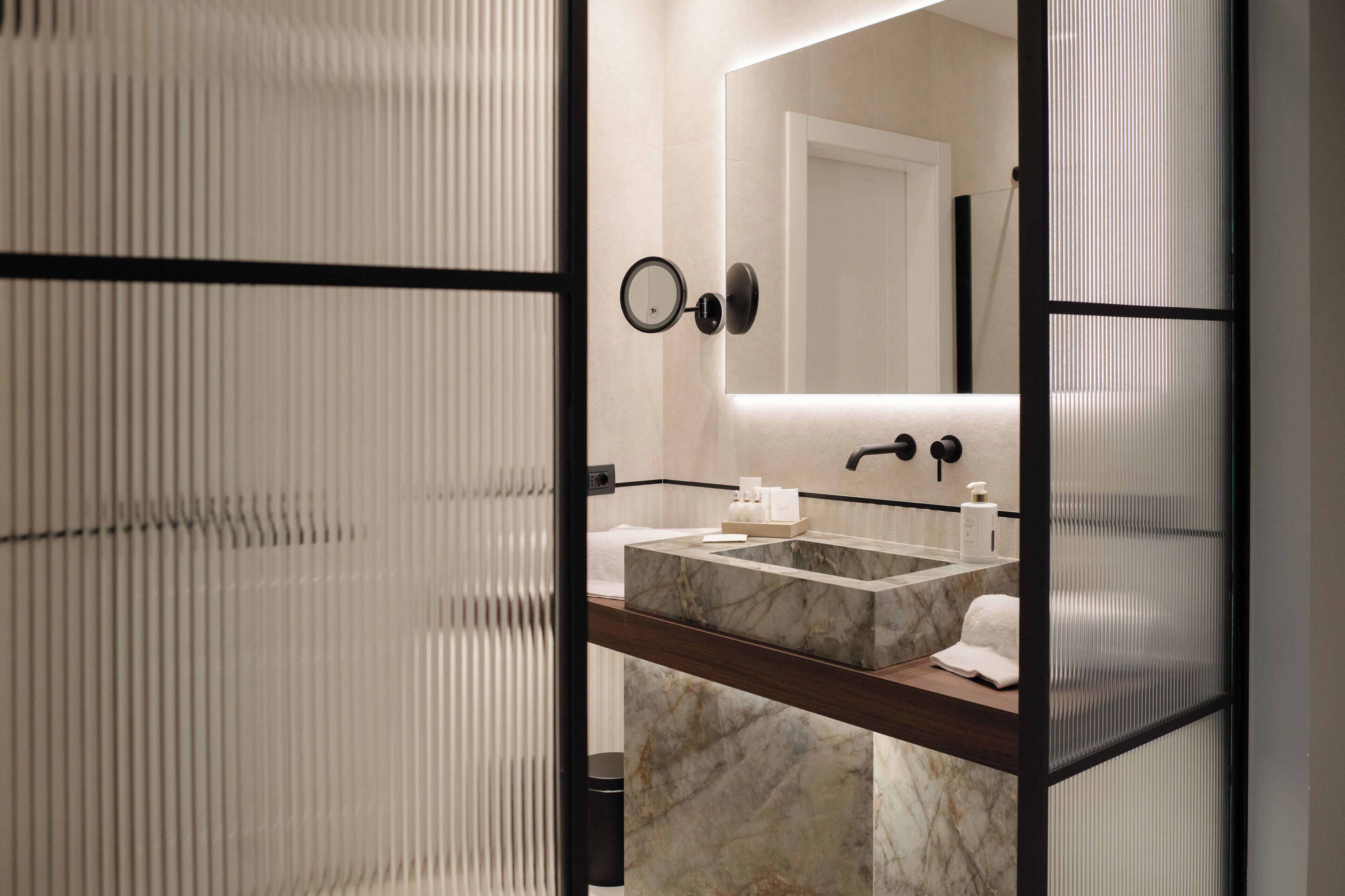 A modern bathroom with a marble sink, a large mirror, and a towel rack.