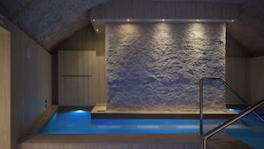 Area benessere con parete in pietra, pavimento in legno e piscina.