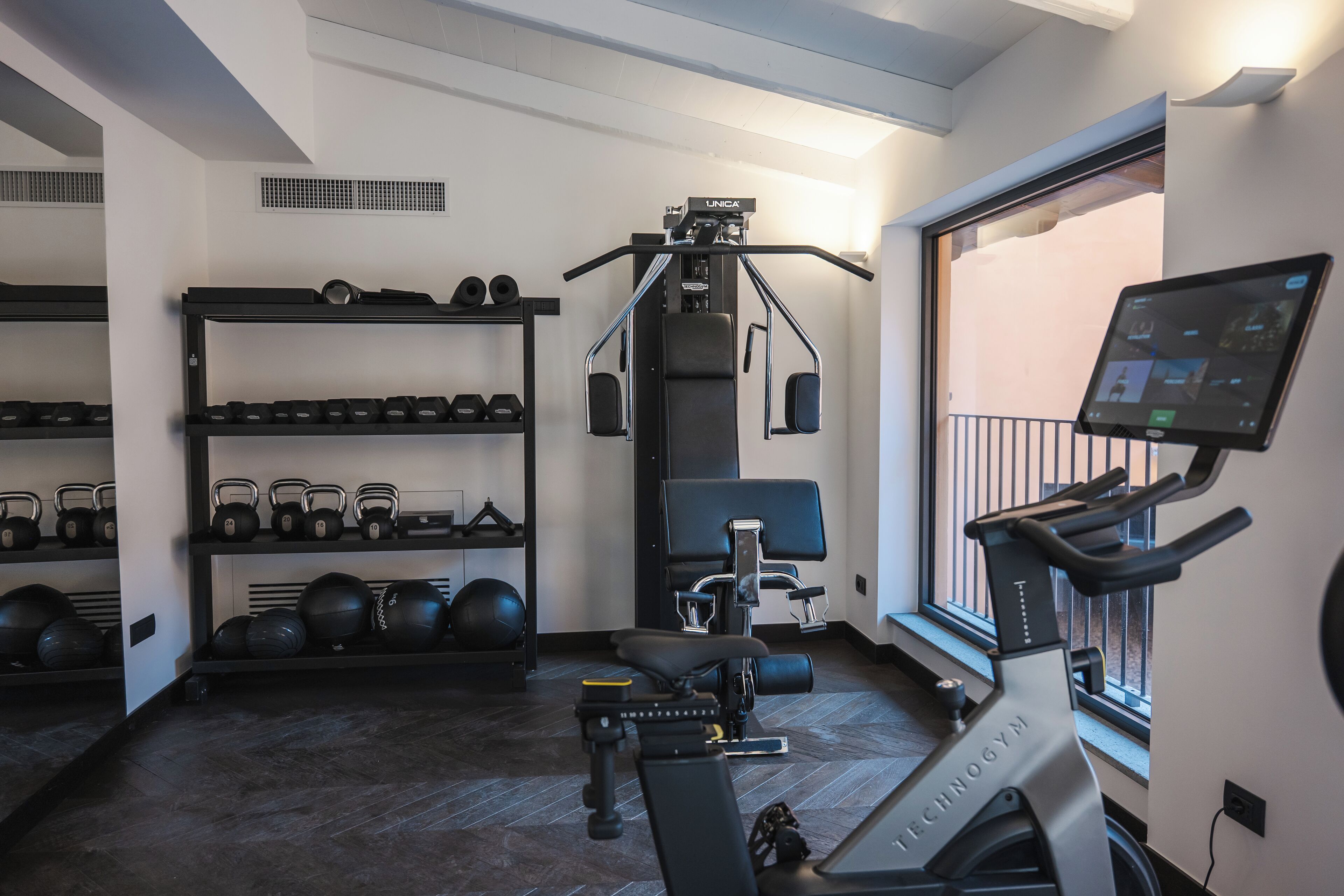Un gimnasio con cinta de correr, máquinas de pesas, kettelbells y un televisor montado en la pared.