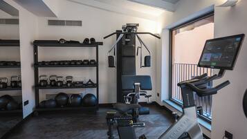 Un gimnasio con cinta de correr, máquinas de pesas, kettelbells y un televisor montado en la pared.