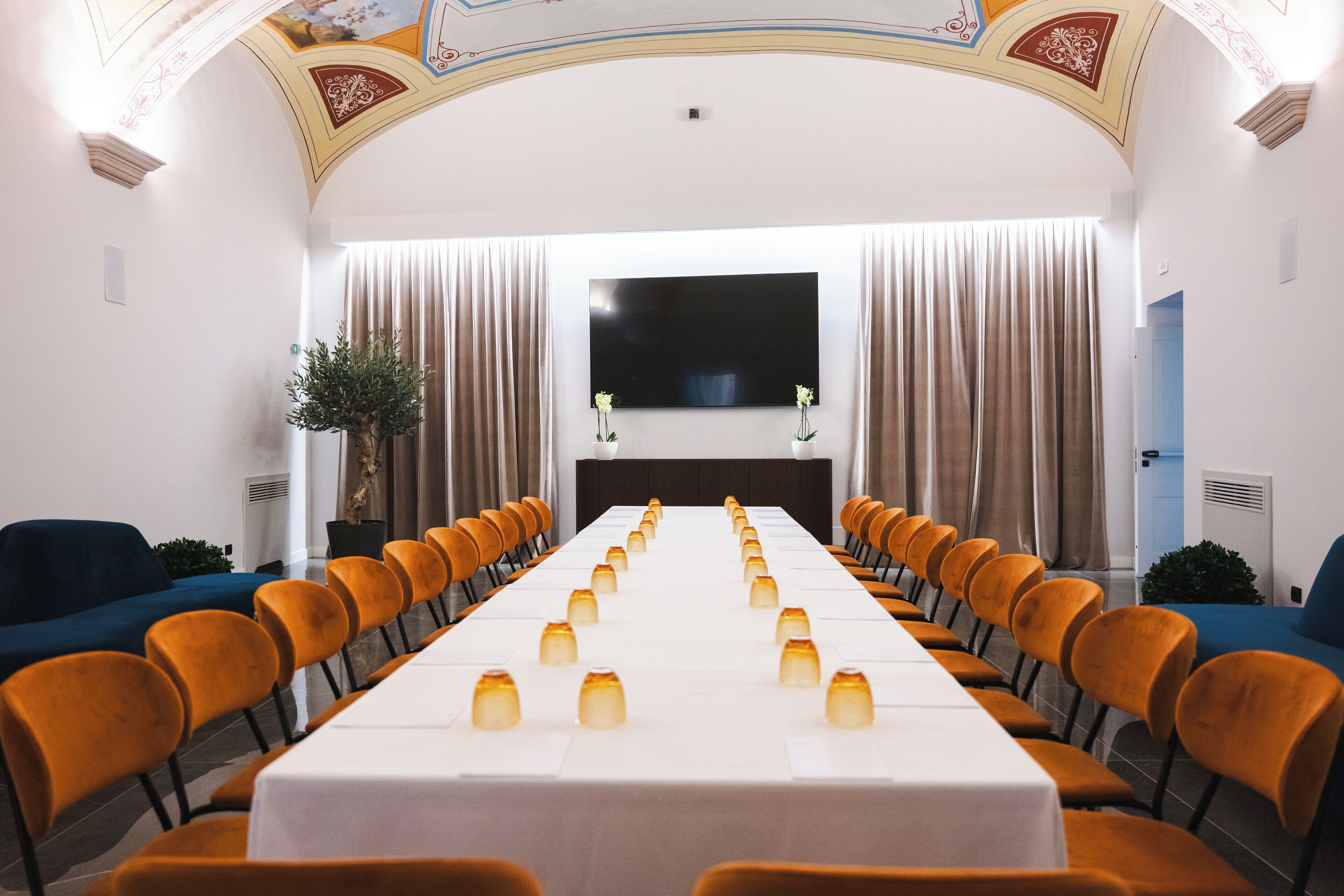 Une salle de conférence avec une longue table, des chaises orange et un téléviseur à écran plat fixé au mur.