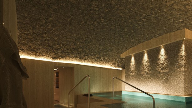 Un'area benessere con piscina, una panca in legno e un appendi asciugamani.