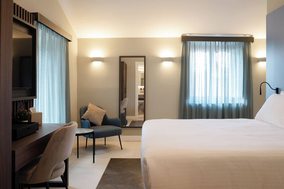 A hotel room with a bed, a desk, a chair, a TV, and a mirror.