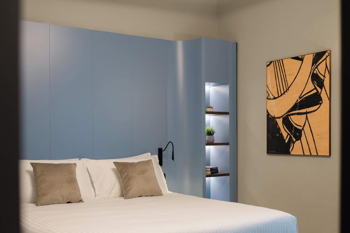 A modern bedroom with a bed, built-in shelving, and a wall-mounted artwork.